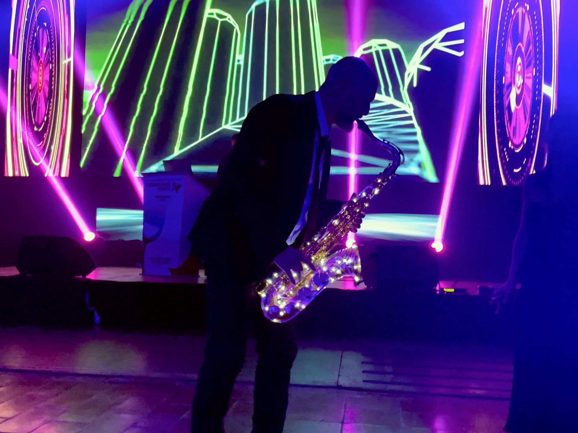 Saxophoniste sur scène devant un décor néon lors d'une soirée
